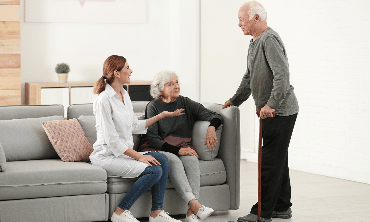 Una cuidadora interna dialoga con una pareja de ancianos en su hogar, reflejando la dedicación del cuidado las 24 horas.